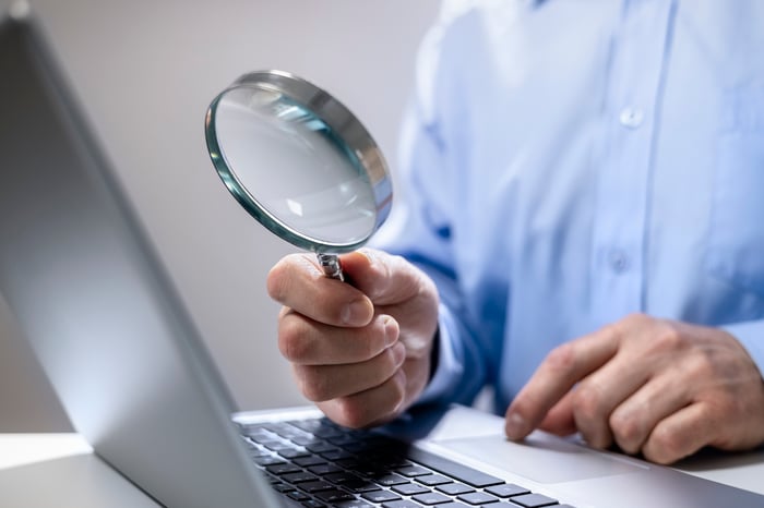 Man holds magnifying glass up to laptop.