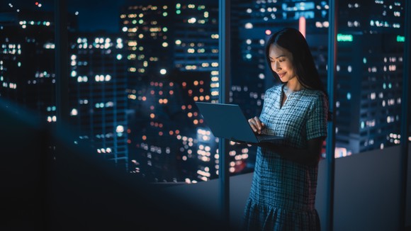 A crypto investor checks her investments on her laptop, set against skyline at night