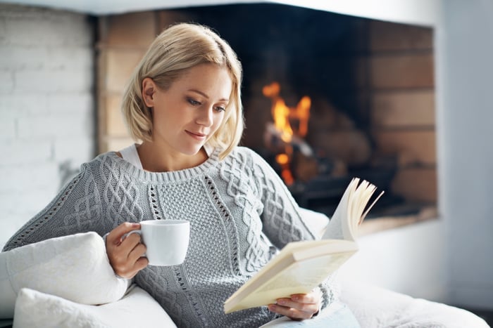 A person holding a mug and reading a book.