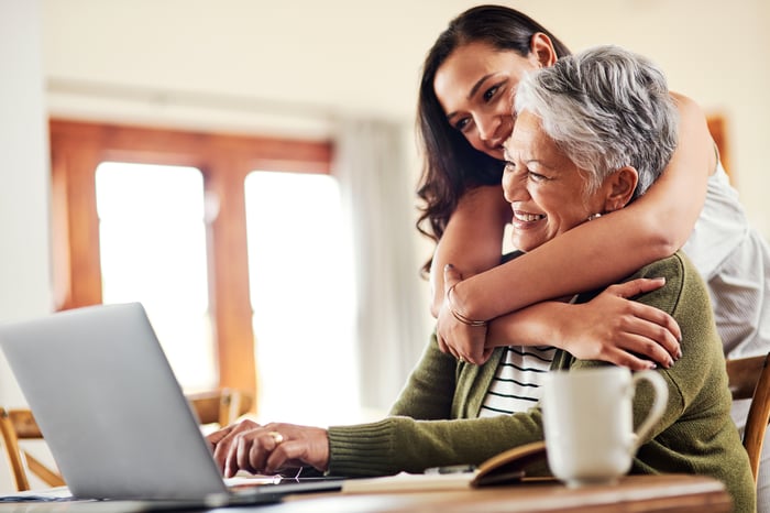 One person hugging another person over the shoulders while they look at a laptop together.