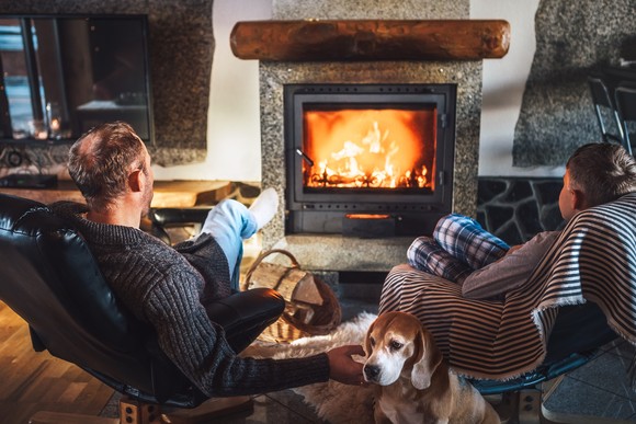 Two people and a dog sitting in front of a fireplace.