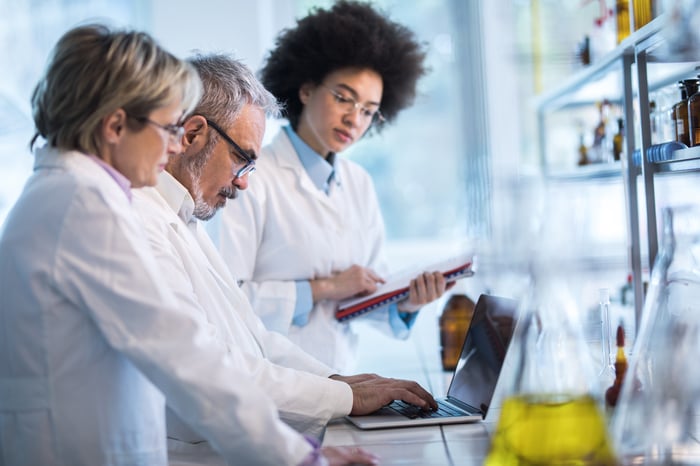 Three researchers in a lab reviewing data on a laptop.