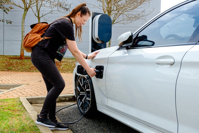 Person charging white electric vehicle.