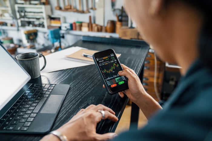 Person using a smartphone to monitor cryptocurrency and stock trading.