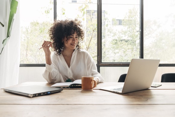 Person behind desk smiling and looking at a laptop screen.