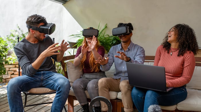 Three people use virtual reality headsets while another individual looks on and laughs.