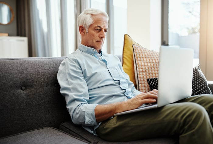 A person typing on a laptop while sitting on a couch.