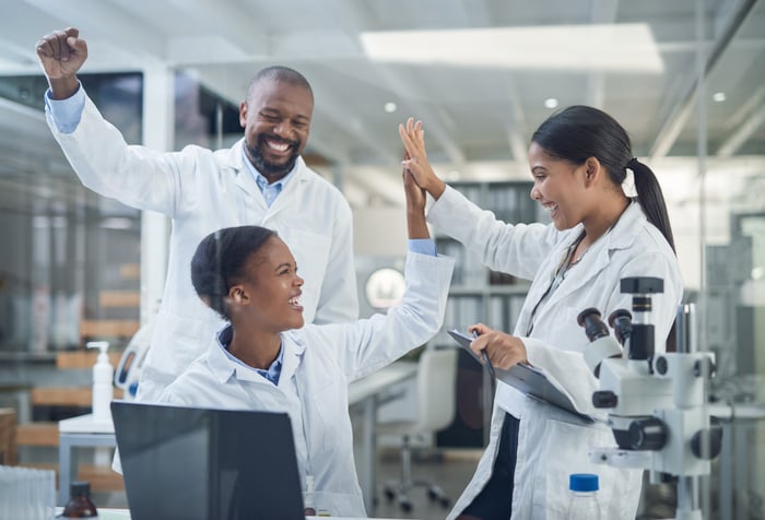 Three lab technicians celebrating with high-fives and fist pumps.