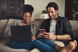 Couple relaxing on couch looking at screens.