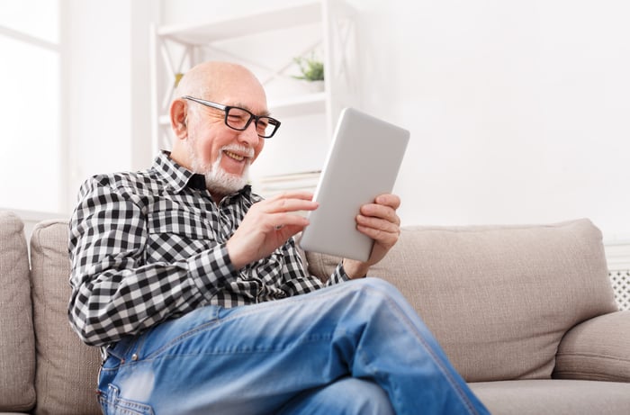 A smiling person on a couch holding a tablet.