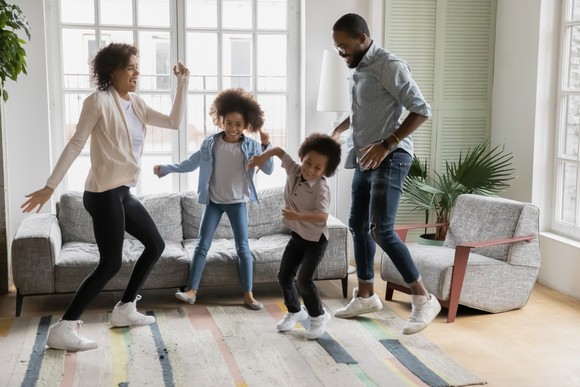 Family of four dancing in a suburban home.