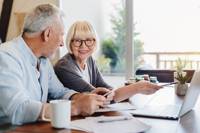 Two seniors looking at  a computer and paper charts together.