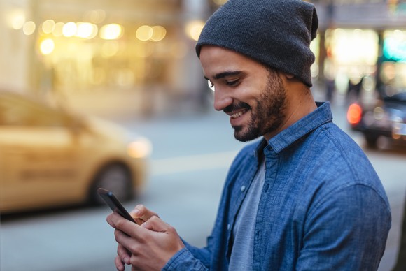 Person standing on urban street checking investments on mobile phone.