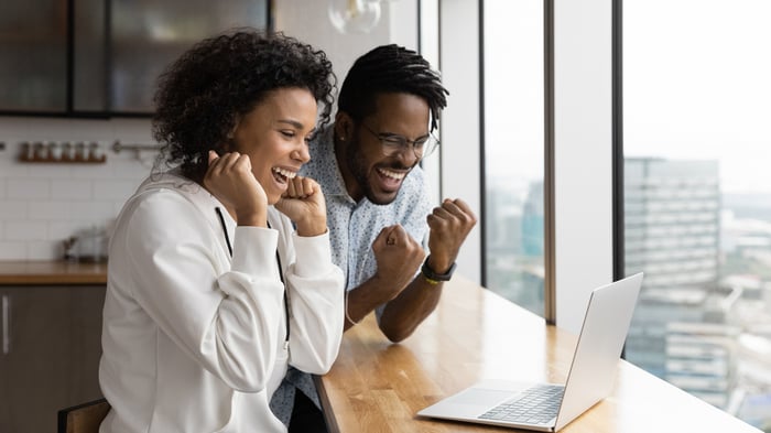 Two people look at a laptop and pump their fists.