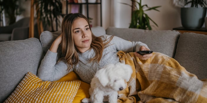 A person and a dog on a couch. The person is holding a remote control.