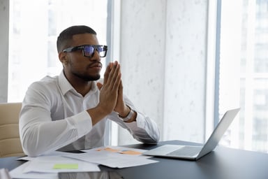 person at laptop holding hands together as if praying