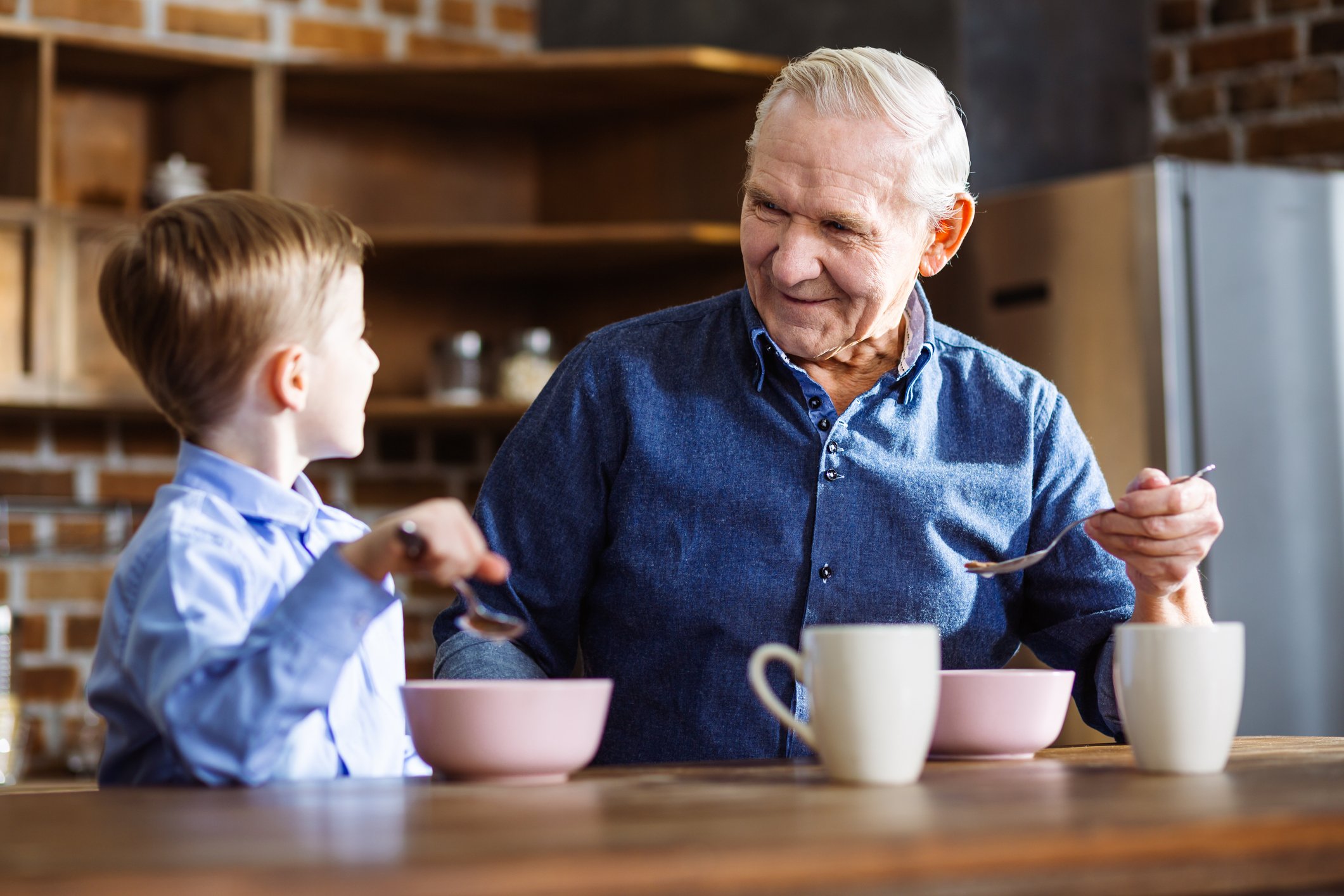 grandparent enjoys breakfast cereal with grandchild in kitchen