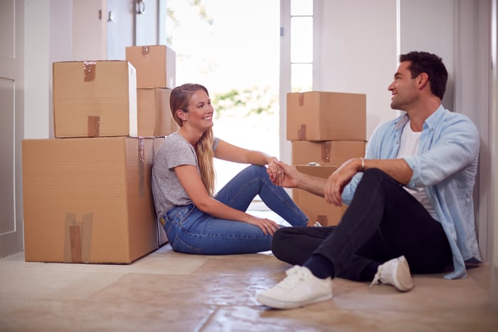 A smiling couple sitting on the floor of their new home, surrounded by boxes.