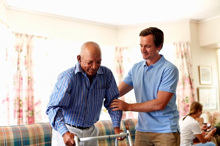 A person helping another person with a walker.