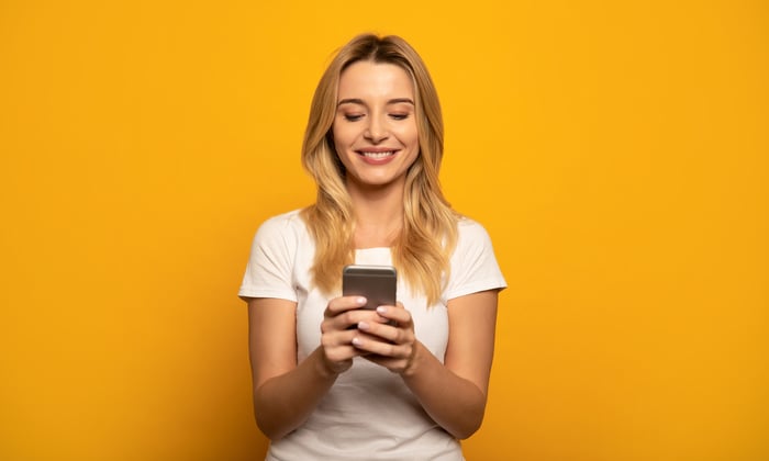 Person looking at phone and smiling in front of a yellow background.