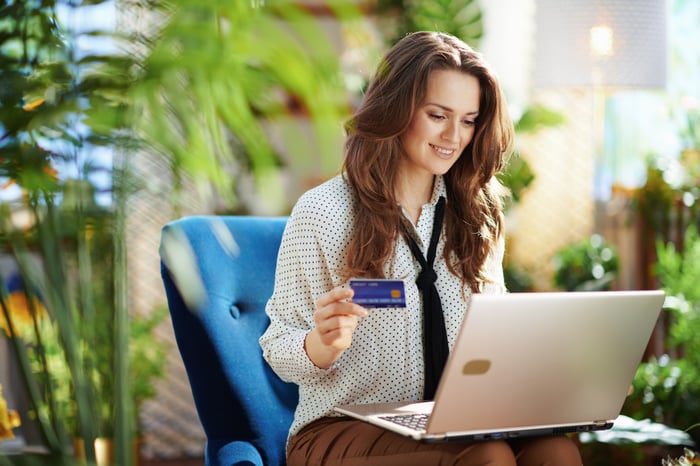 A person holds a credit card while looking at a laptop.