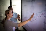 A person pointing to data on a white board.