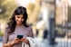 Adult woman walking and texting message on mobile phone outside business center.