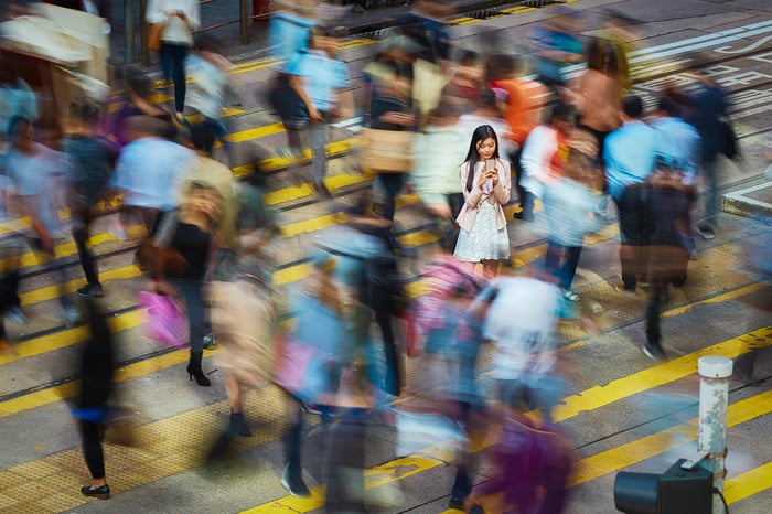A person checks a phone while walking across a crowded crosswalk.