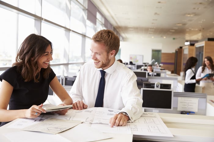 Two professionals consult over papers at a table in an office.