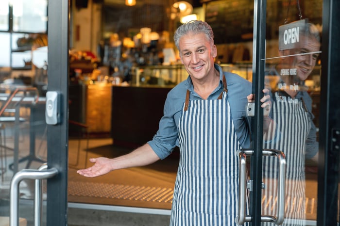 A person in a cafe doorway wearing an apron.