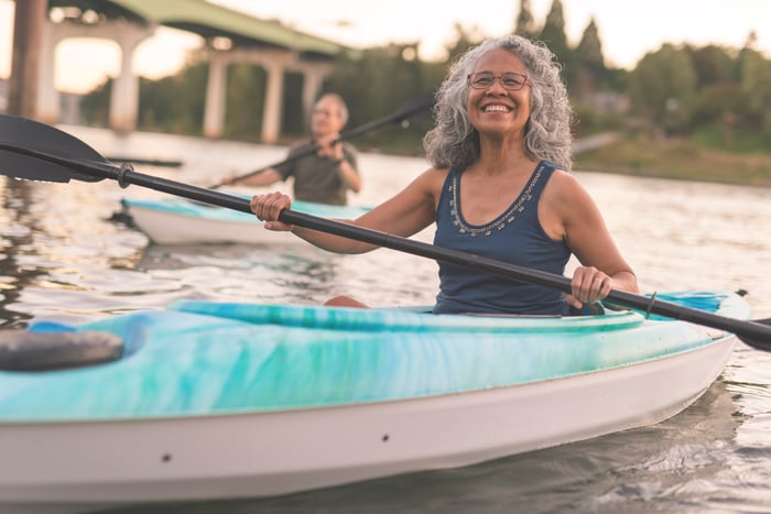 Smiling person wearing glasses kayaks near bridge in a group.