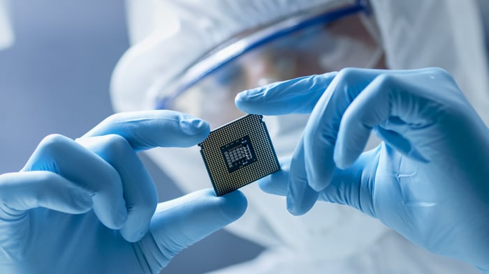 A person wearing a full-body coverall and gloves who's closely examining a microchip. 