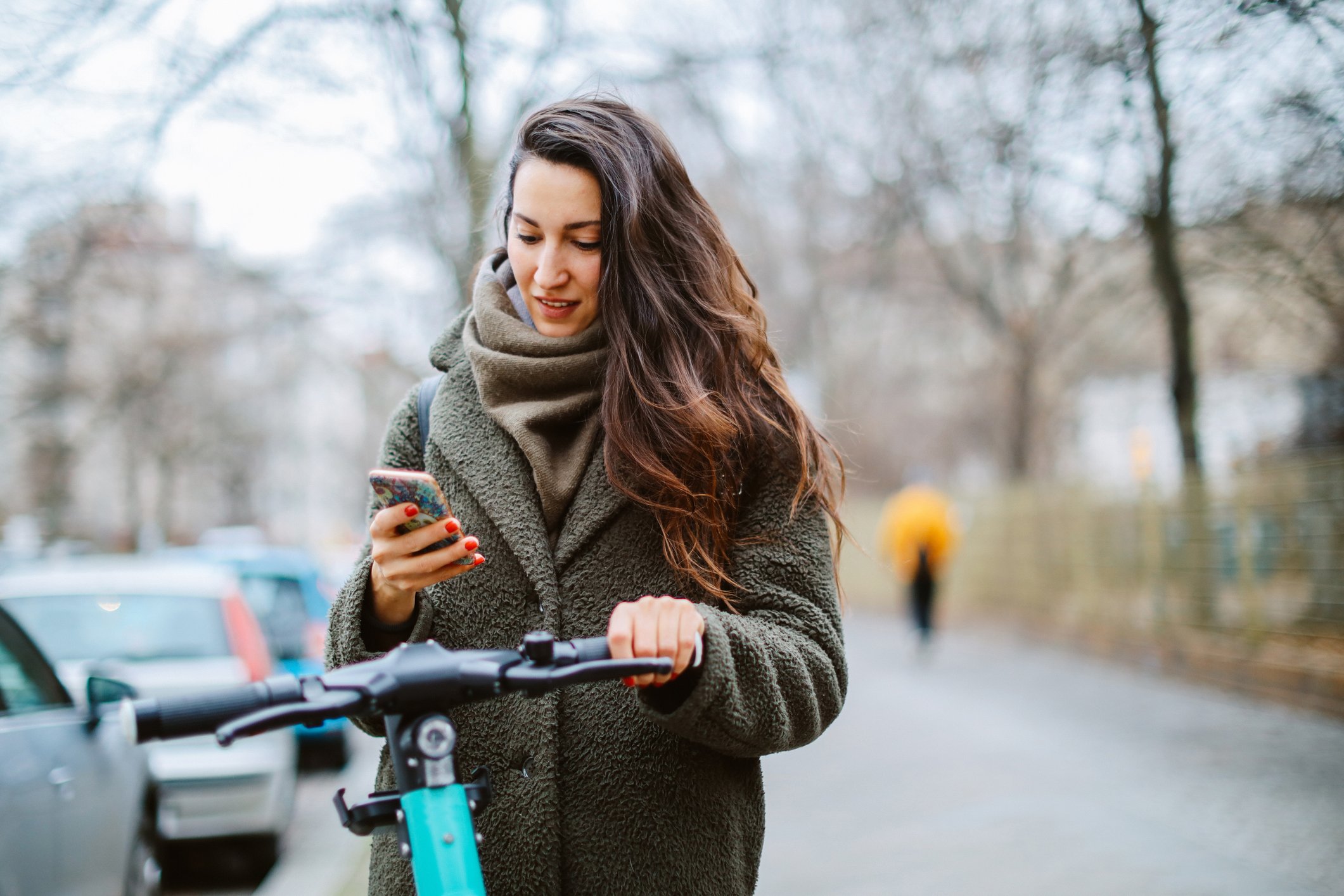A commuter checks a phone while holding an electric scooter.
