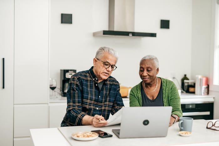 Two people sitting in a kitchen looking at a laptop.