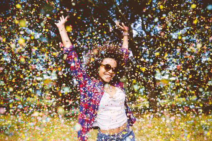 Young person with sunglasses jumping in confetti.