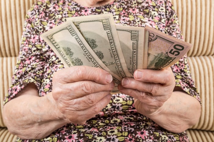 A person holding an assorted pile of fanned cash bills in their hands. 