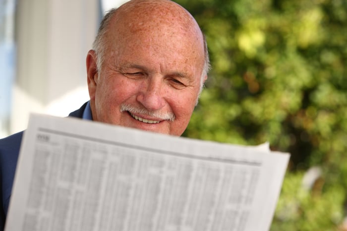 A smiling person reading a financial newspaper. 