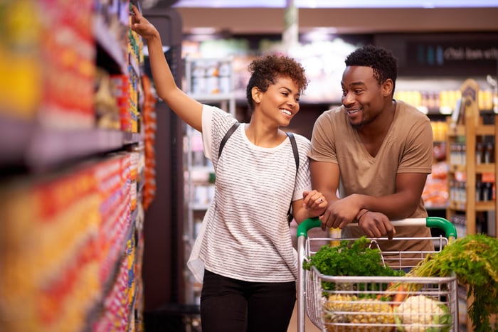 Two people with a shopping cart in a grocery store.