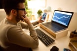 Person deep in thought while looking at a stock chart on a computer.