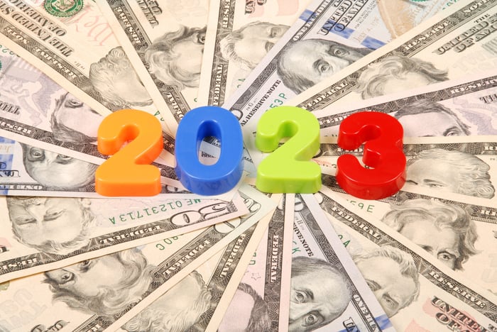 Plastic numbers spelling out 2023 that are placed atop a circular fanned assortment of cash bills.