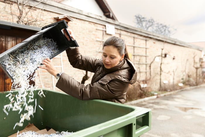 A person dumping shredded documents into a dumpster.