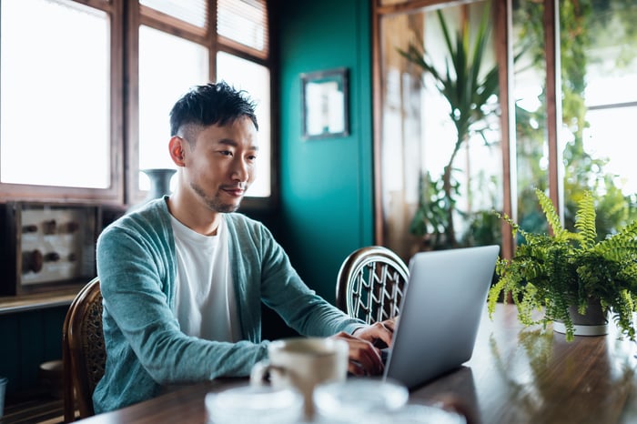 A man sits at home and checks his portfolio on his computer. 