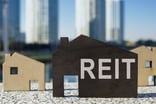 Small wooden cutout of a house with REIT spelled on it.