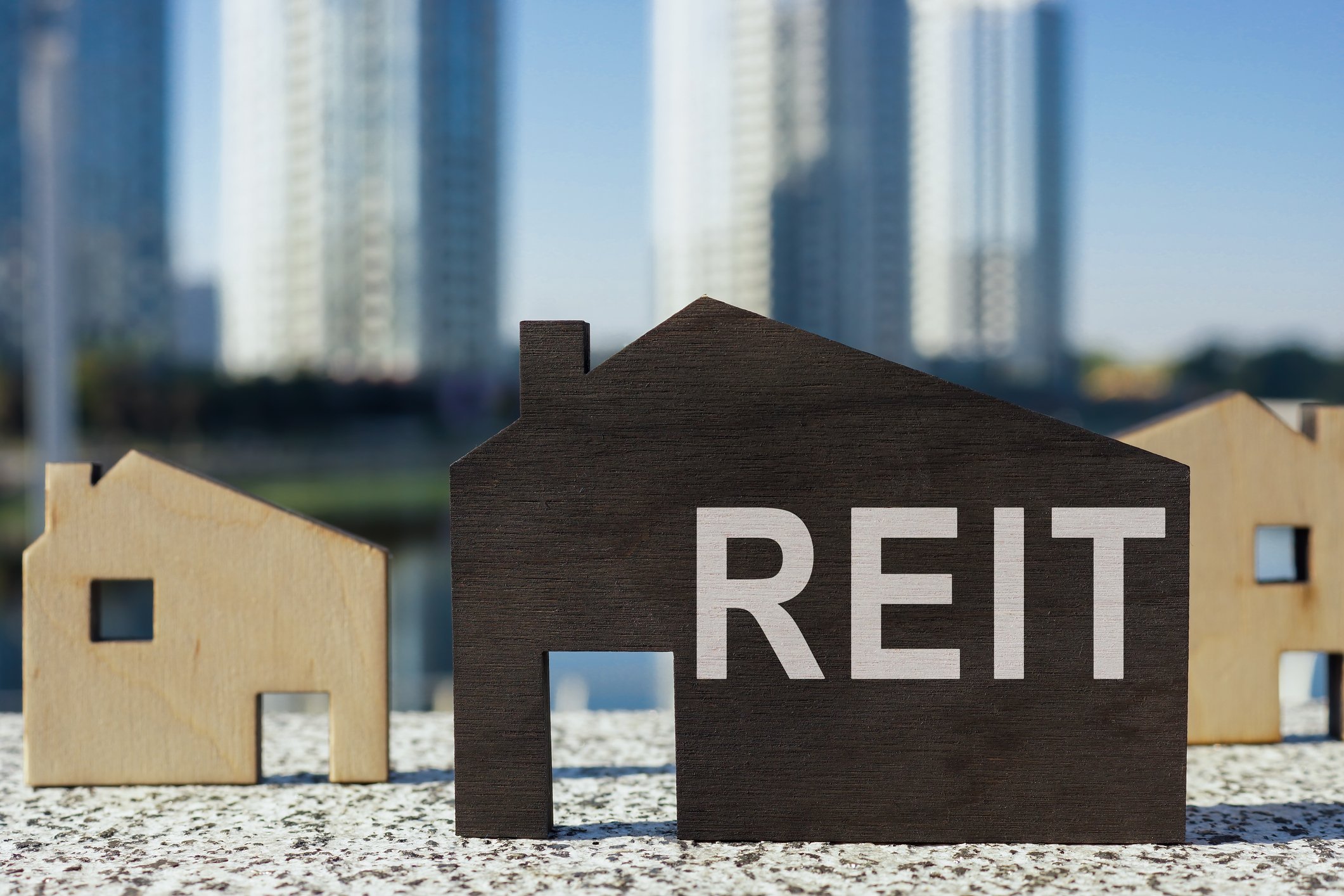 Small wooden cutout of a house with REIT spelled on it.