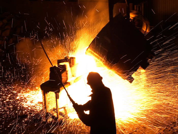 A steel mill with sparks flying and a person in the foreground.