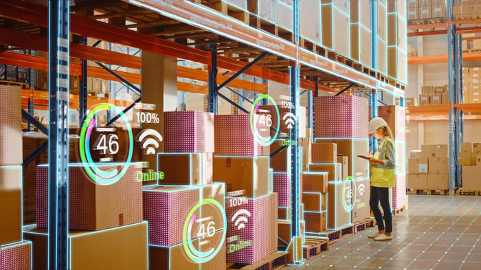 A person standing in front of digitally-enhanced shelving in a large factory.