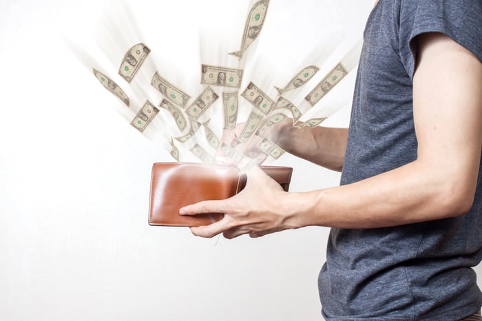 A man opening a wallet and dollar bills flying out of it.