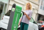 Woman holding electric car charger at a charging station.