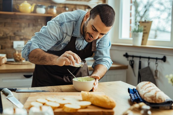 A person smiles while seasoning food in the kitchen.