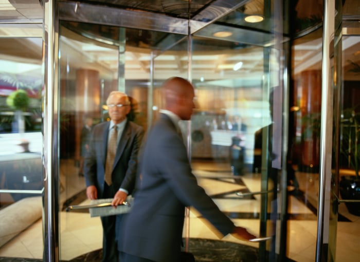 Two people walking through a revolving door.